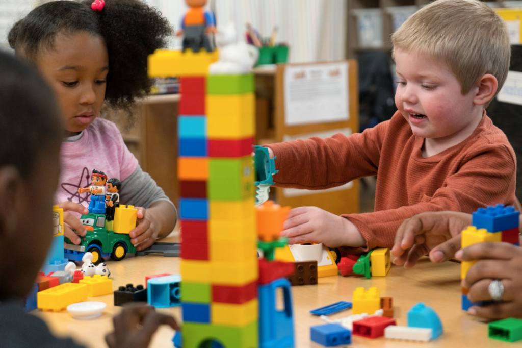 Three pre-k students play and learn with blocks at a table in their classroom.