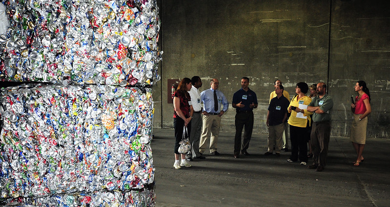 Tour group learns about recycling while standing in front of large bales of crushed metal cans.