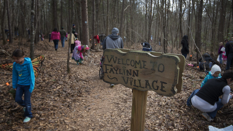 people walking around in woods near sign "Welcome to Faylinn Village."