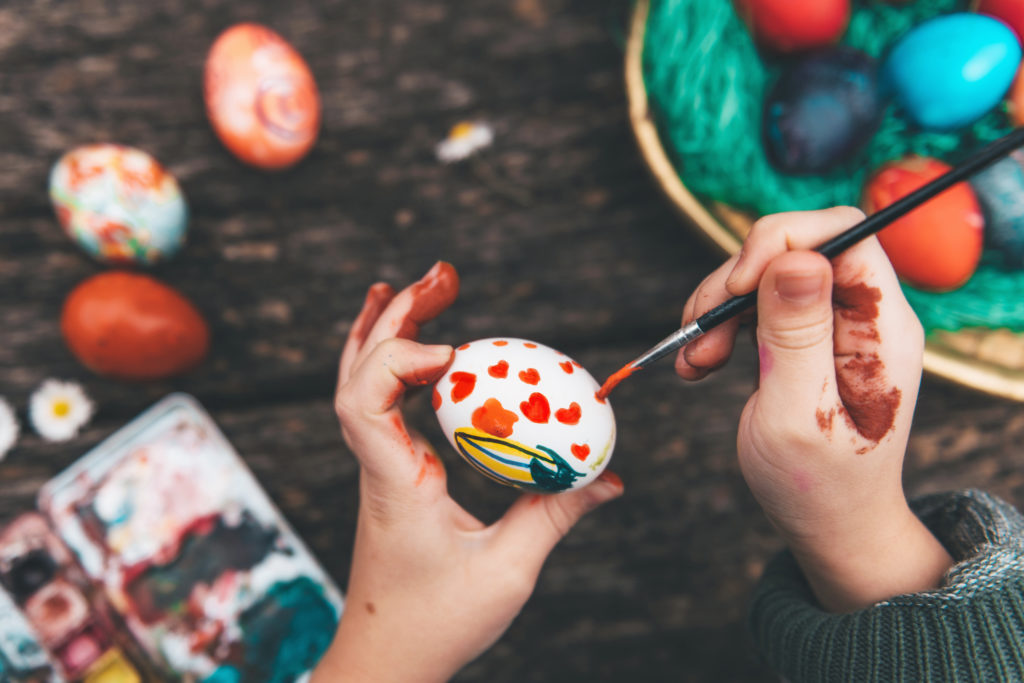 little girl painting easter egg on old wooden table