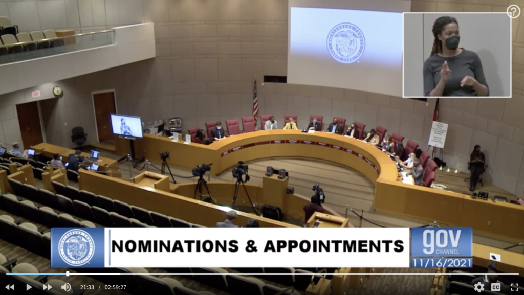 A screenshot from a BOCC meeting that shows the Board sitting at the dais and a picture-in-picture in the top right corner of a sign language interpreter. 