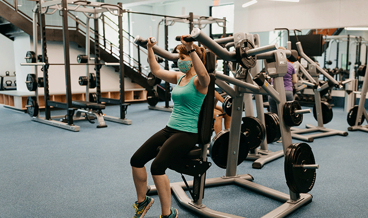 person in a mask using a weight machine at eastway regional recreation center