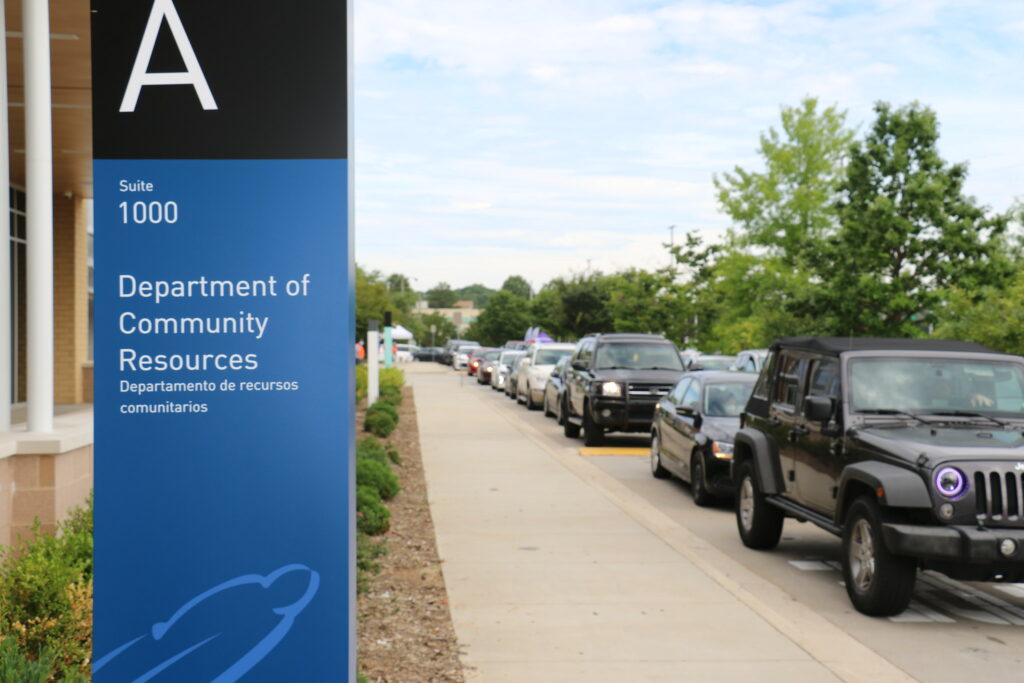 Department of Community Resources sign with a line of cars next to the sidewalk