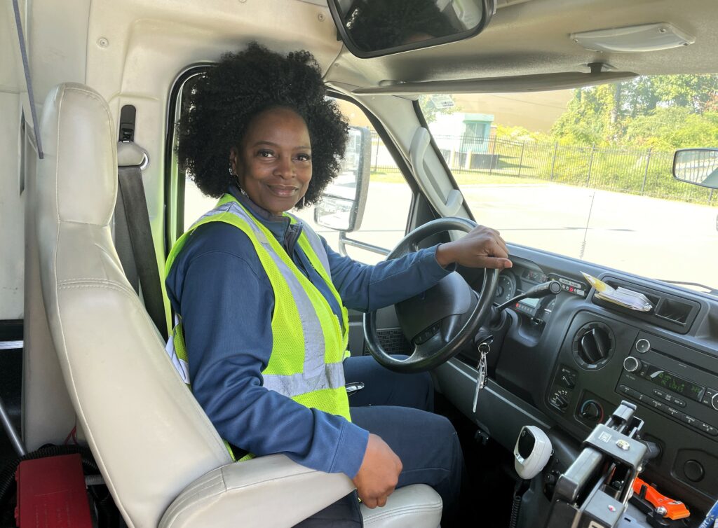 Mecklenburg Transportation Service driver Alison Montgomery, smiling sitting in the driver's seat of a van.