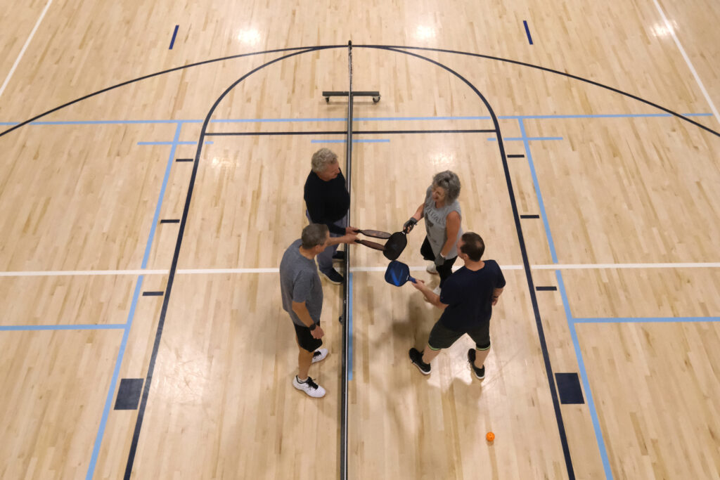 Four people tap their paddles together on an indoor pickleball court.