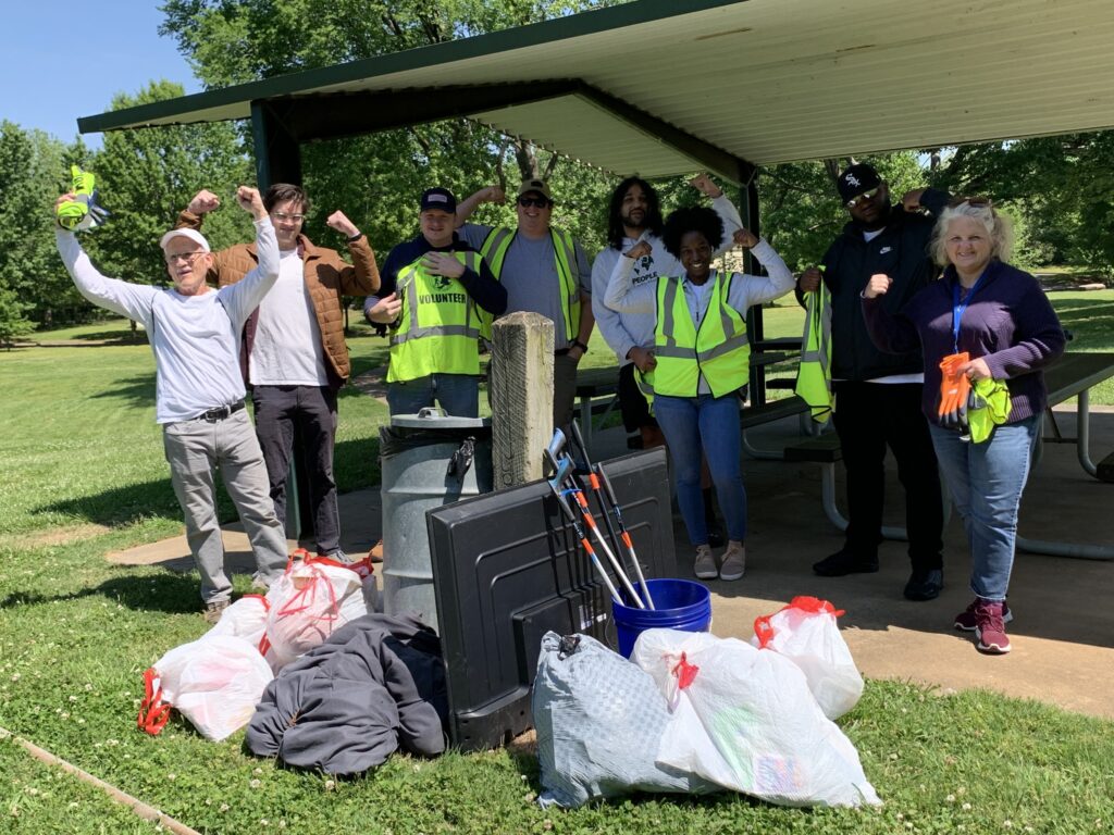 8 volunteers standing in a park behind trash that they picked up in a park